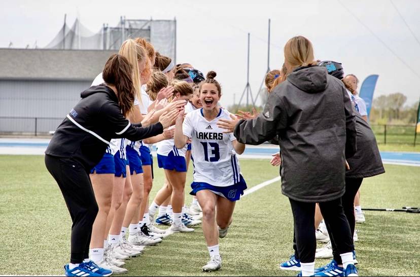Female identifying collegiate lacrosse player running through her teammates giving high-fives